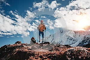 Young tourist walk along high altitude track among snowy and cloudy mountains. Man expeditor with travel backpack going across