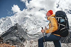 Young tourist walk along high altitude track among snowy and cloudy mountains. Man expeditor with travel backpack going across