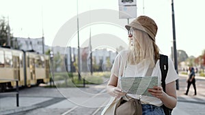 Young tourist woman with backpack searching right direction on map waiting for the public transport at the tram station