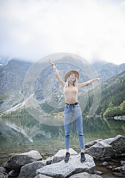 Young tourist woman in a hat with hands up on the top of the mountains