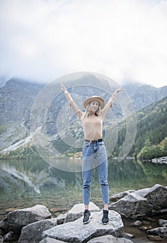 Young tourist woman in a hat with hands up on the top of the mountains