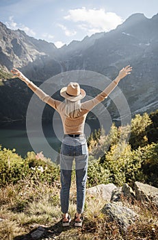 Young tourist woman in a hat with hands up on the top of the mountains