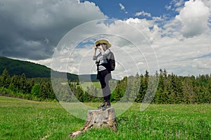 Young tourist woman standing on a tree stump with a camera in hand, making photo pictures