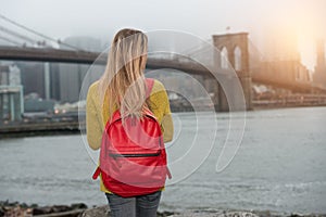 Young tourist woman traveling in New New York city with red backpack and looking to Brooklyn Bridge