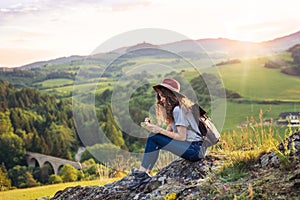 Young tourist woman traveller with backpack sitting in nature, writing notes.