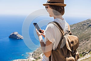 Young tourist woman using smart phone over beautiful landscape with sea at background. Travel, tourism, summer holidays concept