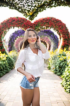 Young tourist woman walking in colorful heart shaped flowers alley in Dubai miracle garden in a sunny day