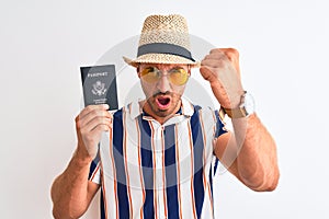 Young tourtist man wearing summer hat and holding USA passport over isolated background annoyed and frustrated shouting with