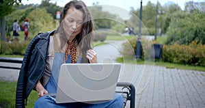 Young townswoman is browsing notebook outside, sitting on bench in park area photo