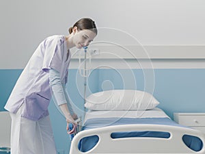 Young trainee nurse working at the hospital and adjusting bed rails