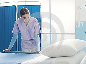 Young trainee nurse working at the hospital and adjusting bed rails
