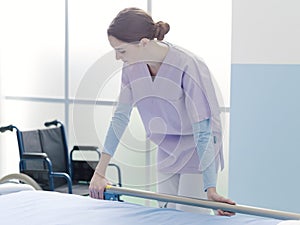 Young trainee nurse working at the hospital and adjusting bed rails