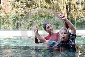 Young trainer helping senior woman in aqua aerobics and working out in the pool. old woman and mature man doing aqua aerobics