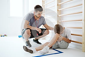 Young trainer helps the injured boy at the school gym