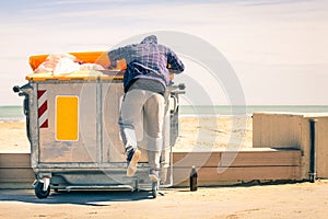 Young tramp rummaging in trash container looking for food and re