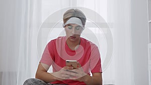 Young transgender homosexual man with makeup and with heapdones sits on fitnes mat and using phone