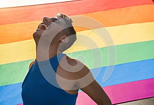 Young transgender man with makeup smiling with lgbt rainbow flag on background