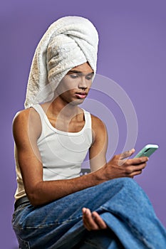Young transgender man in towel looks mobile screen portrait. Muscular model reads morning news
