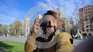 Young travel blogger man having fun and laughing taking a selfie portrait and smiling at Europe city holding a camera on