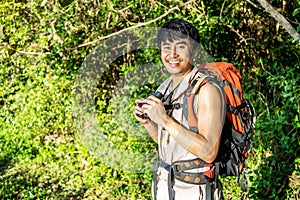 Young travel man relax and enjoy in the Woods, holds binoculars during a camping trip against blue vivid sky