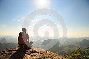 young traveler with backpack sit on the mountain peak rock observing locality