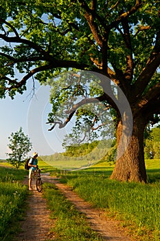 Young traveler with bicycle looking at huge oak