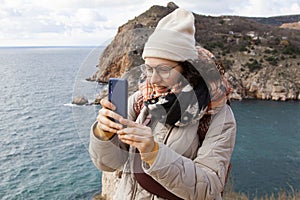A young traveler in glasses for eyesight and curly hair takes pictures on a mobile phone. Using mobile technology