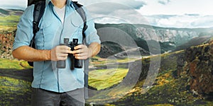 Young Traveler Man With Backpack And Binoculars Seeking Direction In Mountains. Hiking Tourism Journey Concept