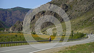 Young traveler man with backpack walking alone on the road on the mountain. Hitchhiker on a road. Travel. 4 k