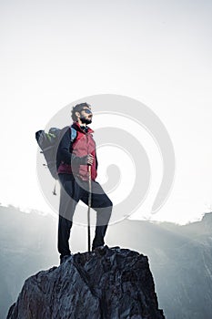 Young traveler in red snow jacket and a backpack standing on blue isolated background. Looking upwards in the sky with confidence