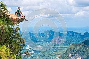 Young traveler sits on a rock that overhangs the abyss, with a beautiful landscape - Khao Ngon Nak Nature Trail in Krabi, Thailand