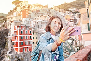 traveler tourist woman taking selfie on her smartphone in famous old italian village Riomaggiore, Cinque Terre, Italy