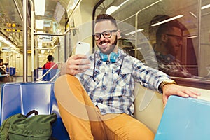 Young traveler wearing plaid shirt and glasses reading fun feeds on social network pages on cell phone on subway metro public