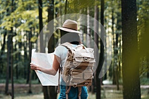 Young traveler woman hold location map in hands among trees in forest and searching directional for traveling