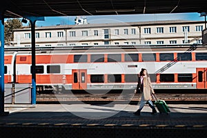 Young traveler woman with luggage waiting for train at train station platform.Train in the background.