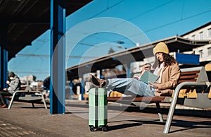 Young traveler woman sitting alone at train station platform with luggage.