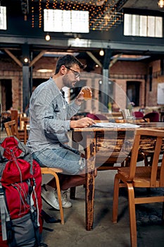 Young traveling man on a coffee stop, enjoying drink and reading newspaper alone at a cafe