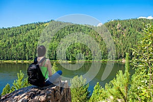 Young traveling woman sitting on the top of the mountain cliff.