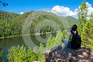 Young traveling woman sitting on the top of the mountain cliff.