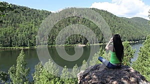 Young traveling woman sitting on the top of the mountain cliff.