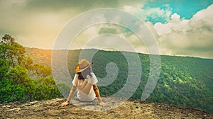 Young traveling woman wearing hat and sitting on the top of the mountain cliff with relaxing mood. Asian woman travel alone.