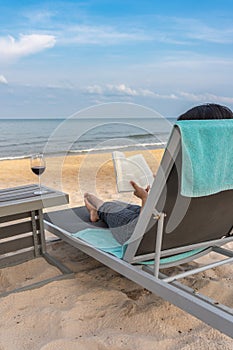 Traveller reading book with glass of wine on beautiful beach