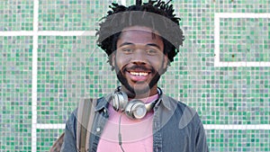 A young trendy black male student with dreadlocks standing outside a cool wall. Portrait of a happy stylish African man