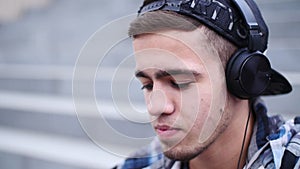 Young trendy man listen to music on smartphone sitting on the steps outdoor