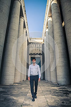 Young trendy man walking through the ancient columns of a historic building.