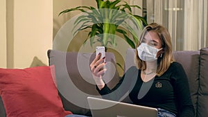 Young Turkish woman with a facial mask, having a video call on her smartphone while sitting on the sofa.