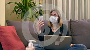 Young Turkish woman with a facial mask, having a video call on her smartphone while sitting on the sofa.