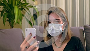 Young Turkish woman with a facial mask, having a video call on her smartphone while sitting on the sofa.