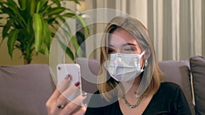 Young Turkish woman with a facial mask, having a video call on her smartphone while sitting on the sofa.