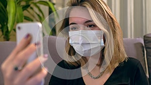 Young Turkish woman with a facial mask, having a video call on her smartphone while sitting on the sofa.